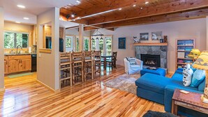 A spacious living area with a wooden floor, a blue sofa, a fireplace, and a dining area with wooden chairs and a table.
