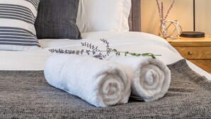 A neatly made bed with rolled towels, a striped pillow, a gray pillow, and a bedside lamp with a decorative item beside it. - 2 King Beds, Quiet Neighborhood, Near It All (Tigard)