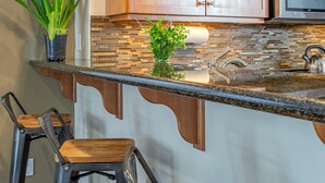 A kitchen with wooden cabinets, a stainless steel microwave, a granite countertop, and two bar stools. - 2 King Beds, Quiet Neighborhood, Near It All (Tigard)