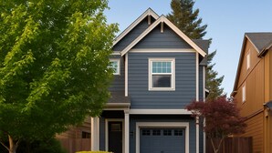 A two-story house with a dark blue exterior, a front garage door, and a small front yard with a tree and a bush. - 2 King Beds, Quiet Neighborhood, Near It All (Tigard)