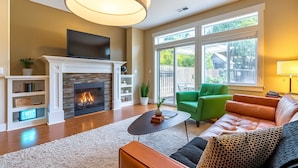 A living room with a fireplace, a television, a sofa, a coffee table, and a large window. - 2 King Beds, Quiet Neighborhood, Near It All (Tigard)