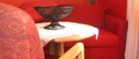 A room with a red sofa, a wooden chair, a small table with a bowl, and a hanging lamp.