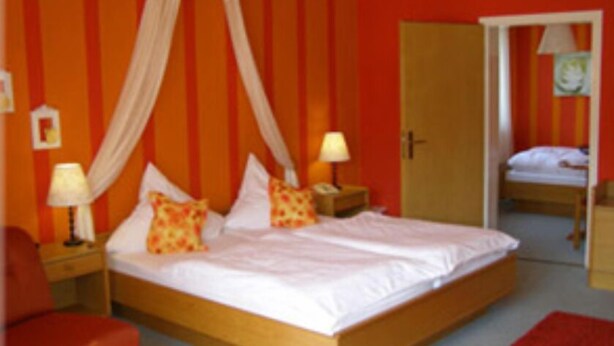 A room with a bed, two bedside tables with lamps, a red chair, and a door leading to another room. - Gasthaus & Pension Koch (Cursdorf)