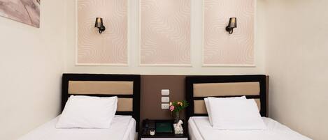 A hotel room with two beds, a nightstand with a phone, a vase with flowers, and wall-mounted lamps.