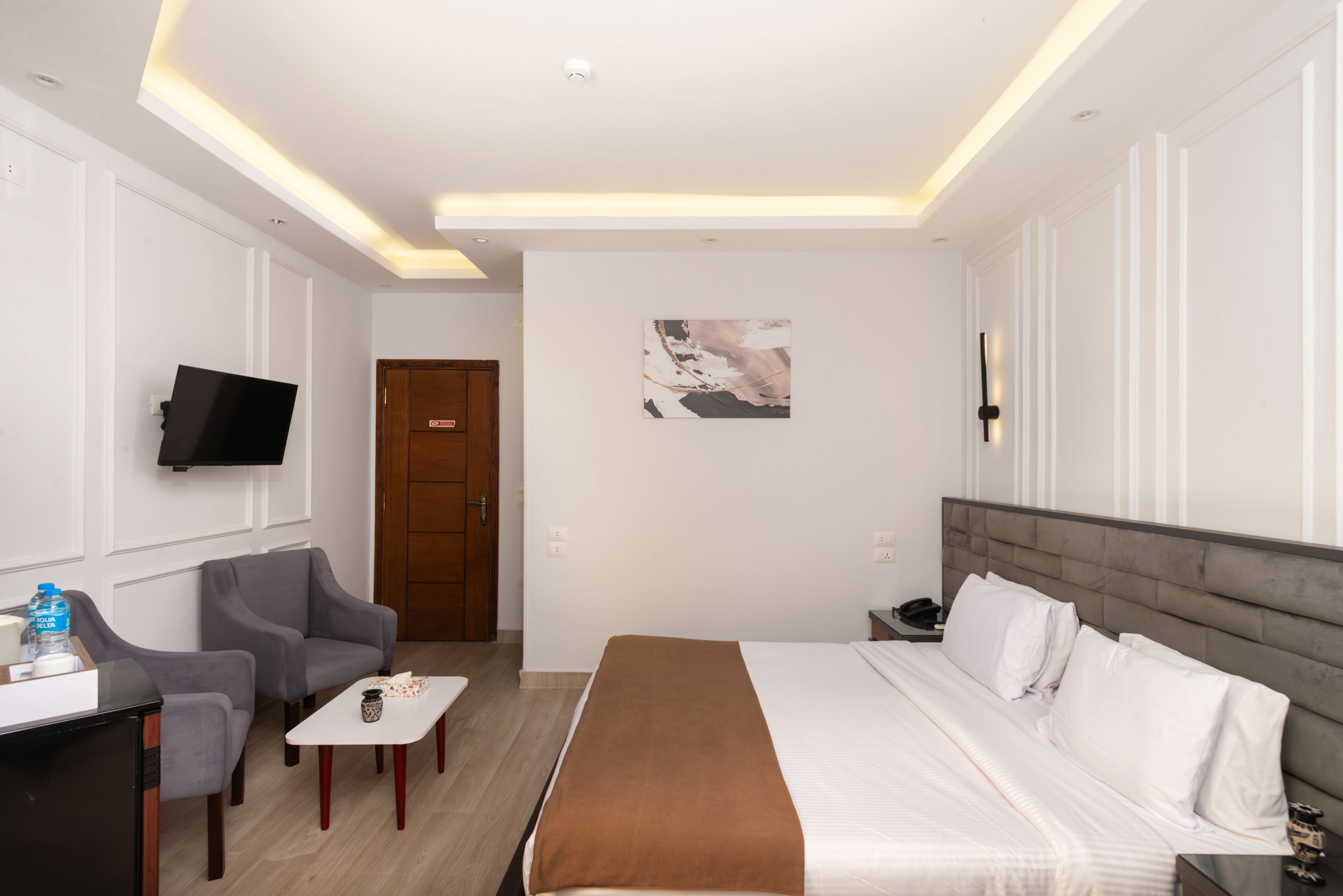 Een hotelkamer met een bed, een bureau met stoel, een aan de muur bevestigde televisie en een deur.
