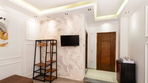Un salon moderne avec un téléviseur à écran plat fixé au mur, une étagère en forme d’échelle en bois, un banc marron et une porte en bois donnant sur une autre pièce.
