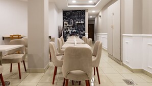 Un espace repas moderne avec des tables et des chaises blanches, un mur noir où sont écrits des textes sur le thème du café, et un design épuré et minimaliste.