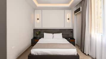 Een moderne hotelkamer met een groot bed, nachtkastjes, een wandairconditioner en een raam met gordijnen.