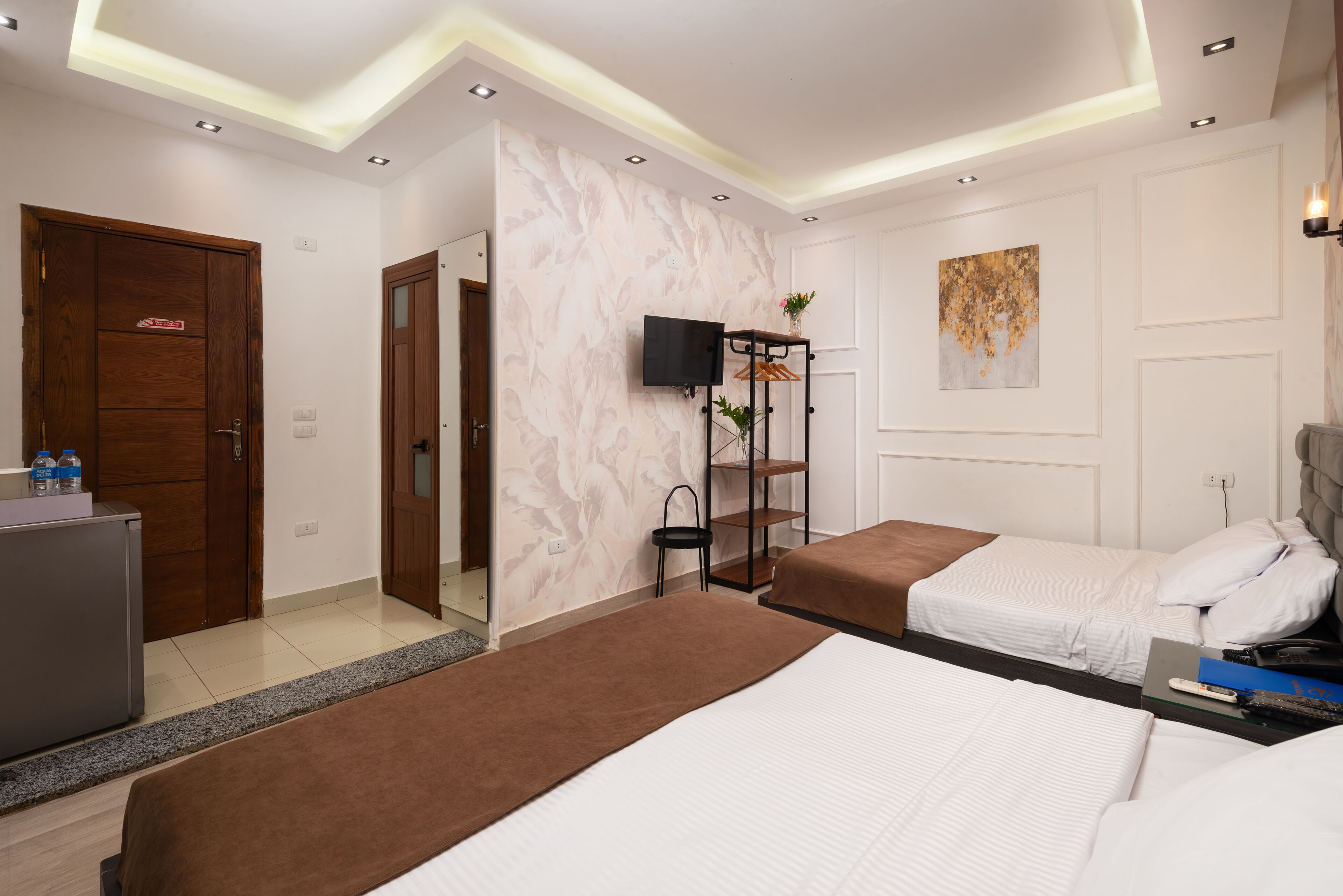 A hotel room with two beds, a TV, a small table with a plant, and a mirror.