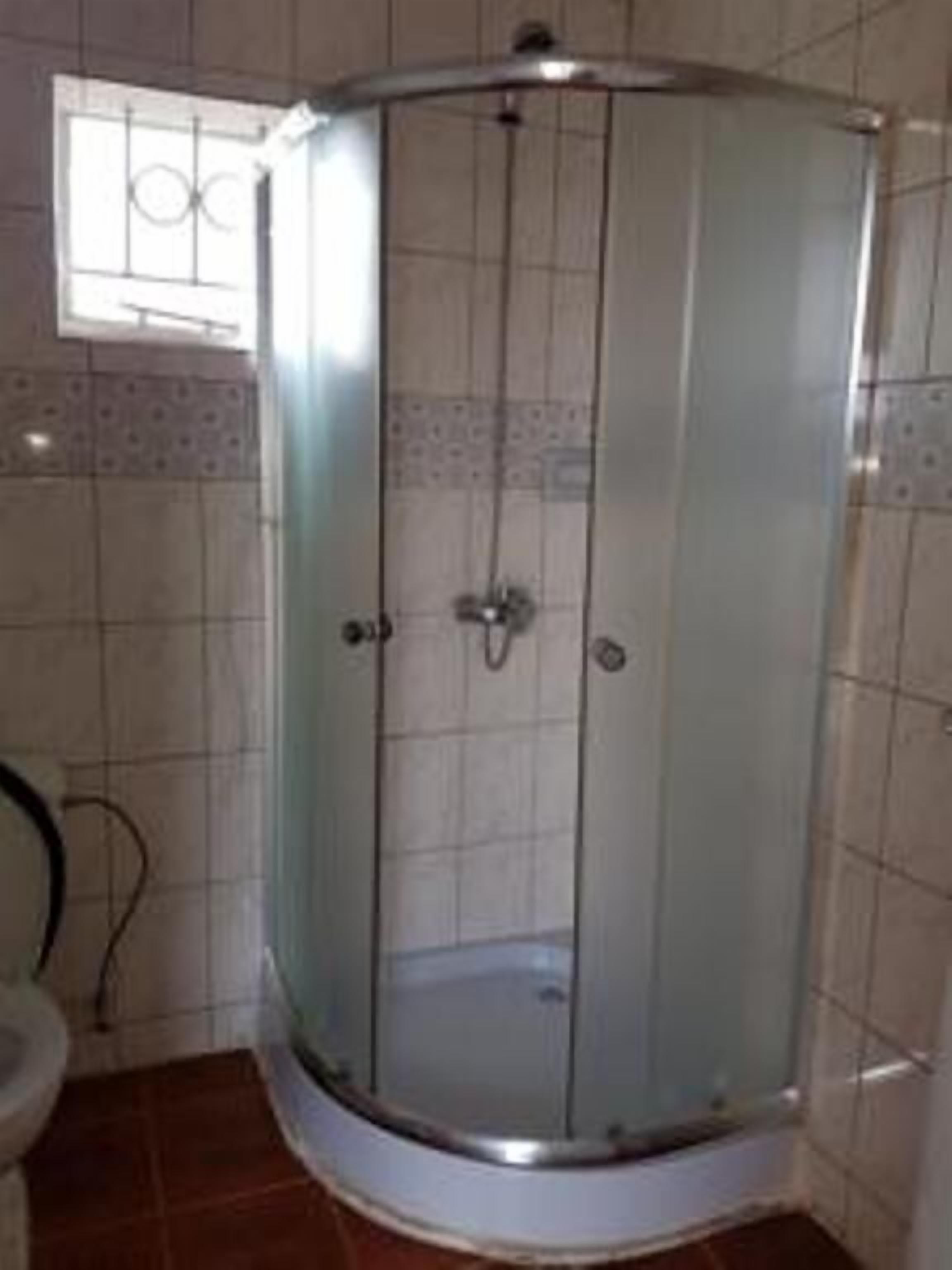 Cabina de ducha con paredes de vidrio, suelo de baldosas y una ventana arriba.