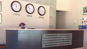 A reception desk with clocks labeled 'Livingstone,' 'London,' and 'New York.' - Mopees Lodge (Choma)