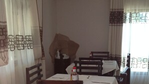 A dining area with wooden chairs and tables, a bottle of ketchup, and a large decorative item on the wall. - Mopees Lodge (Choma)