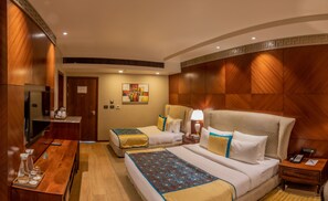 A hotel room with a wooden headboard, two beds, a desk with a telephone, and a painting on the wall.