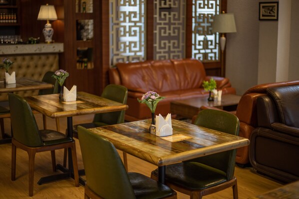 Un restaurante acogedor con mesas de madera y sillas verdes, un sofá de cuero y lámparas decorativas.