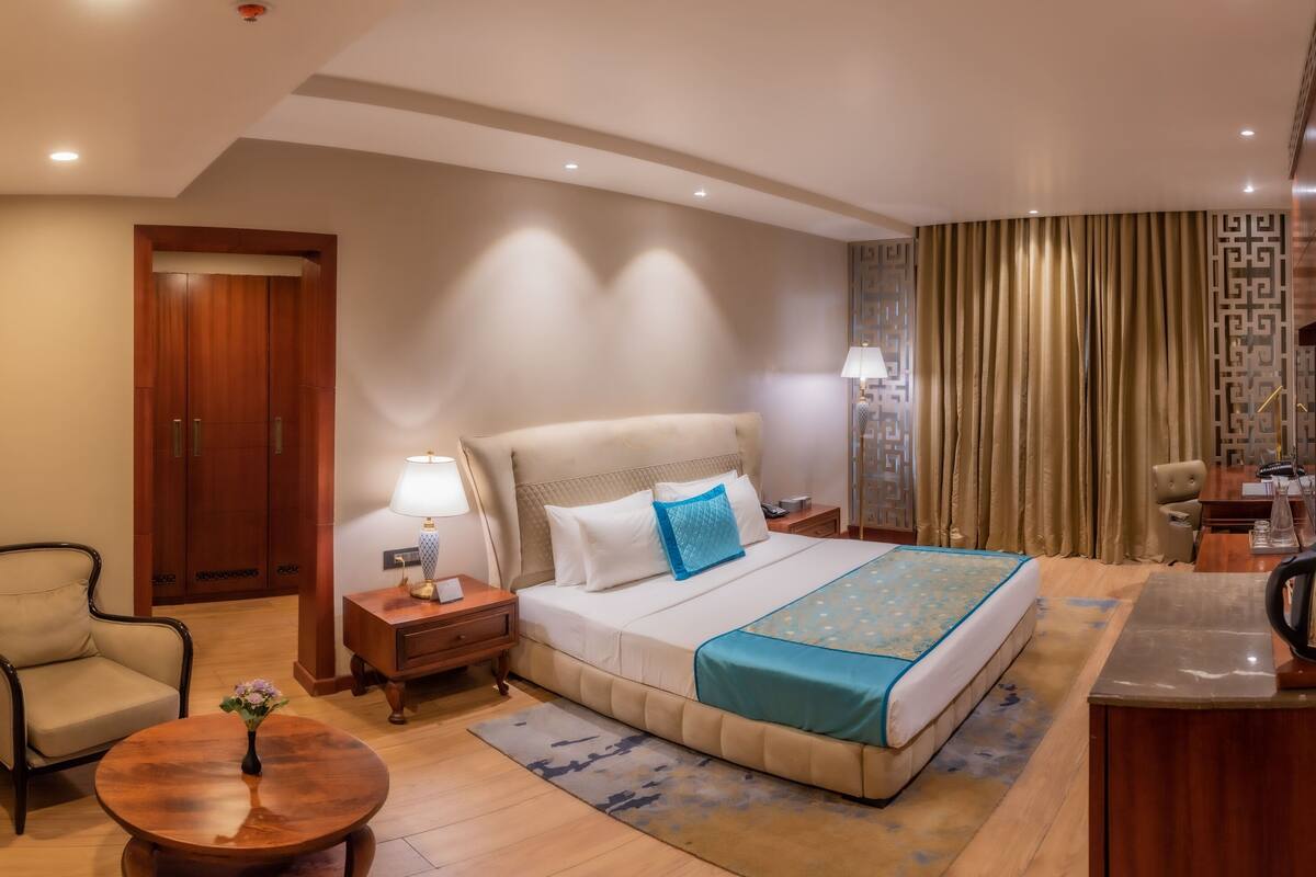 Ein Hotelzimmer mit Bett, Nachttisch, Lampe, Stuhl und einem kleinen Tisch mit einer Vase.