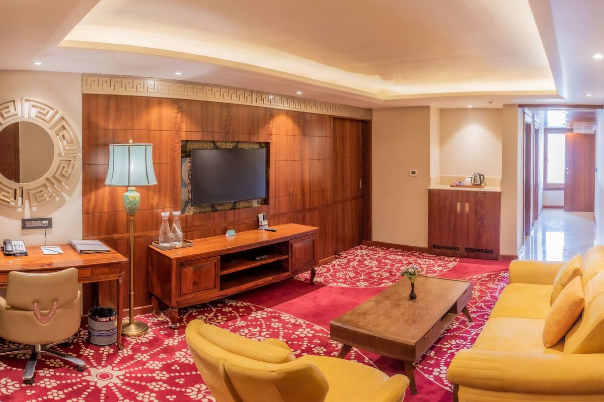 Ein modernes Wohnzimmer mit Fernseher, Holzvertäfelung, Schreibtisch mit Lampe, Couchtisch und gelben Sofas.