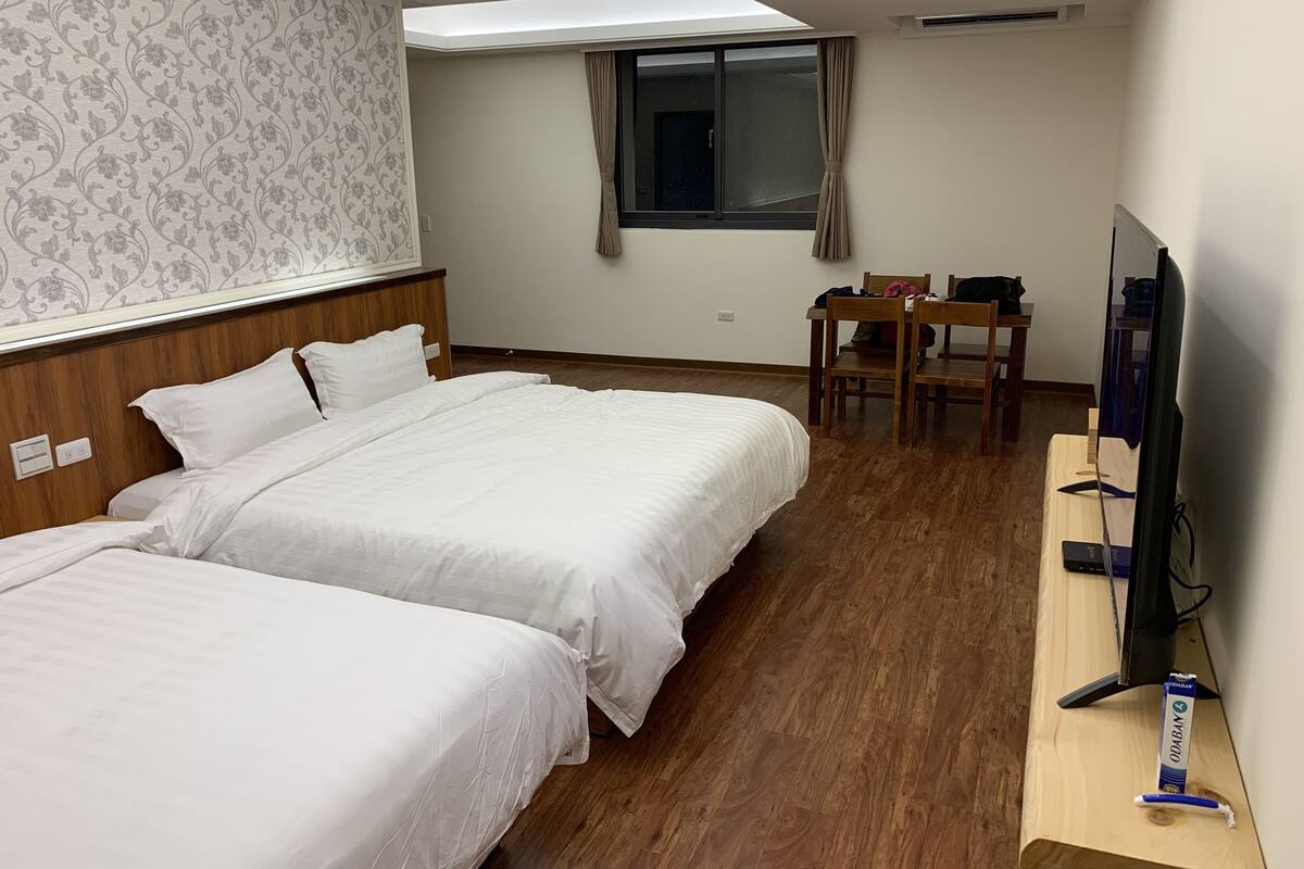 A hotel room with two beds, a desk, a television, and a window with curtains.