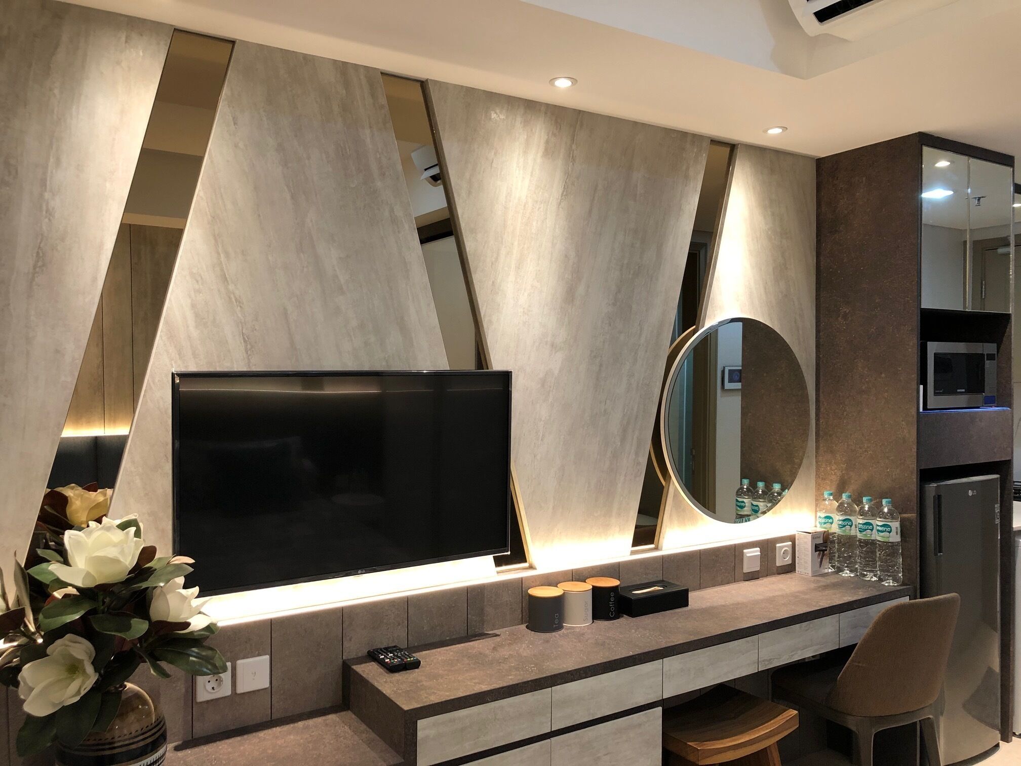 A modern living room with a large flat-screen TV, a round mirror, and a coffee station.