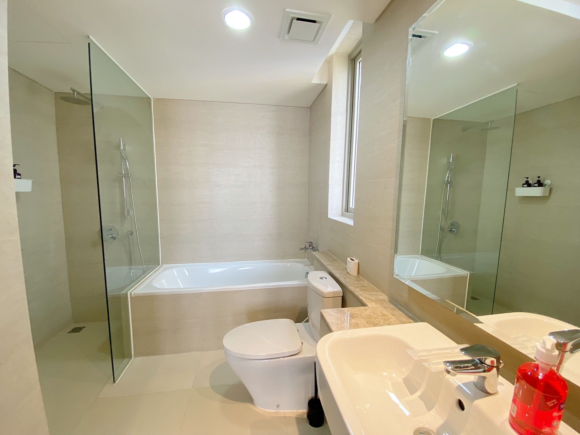 A modern bathroom with a glass-enclosed shower, a white toilet, a bathtub, and a sink with a mirror.