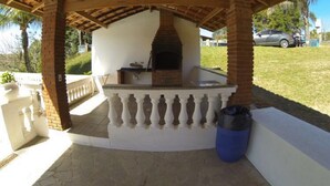 Un espace de cuisson extérieur abrité, doté d’un four en briques, d’une balustrade blanche et d’une poubelle bleue.