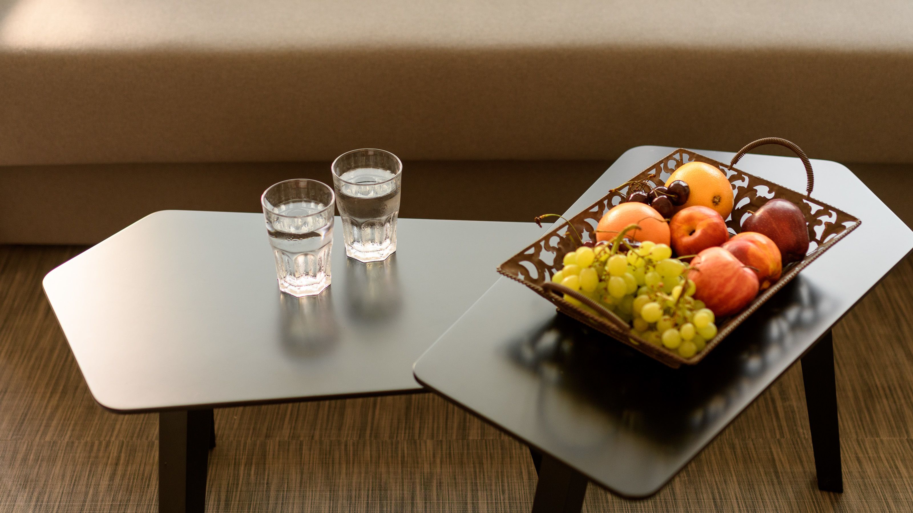 A small table with two glasses of water and a fruit basket.