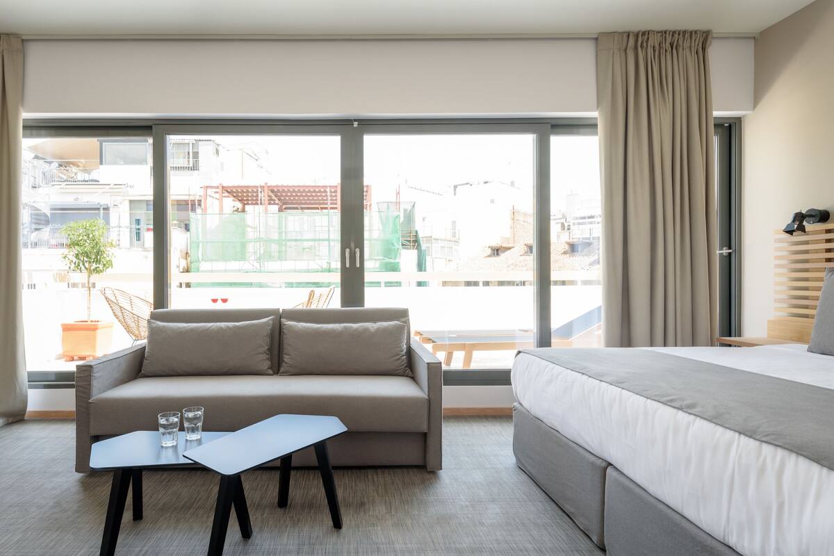 A hotel room with a bed, a sofa, a small table, and a view of the outside.