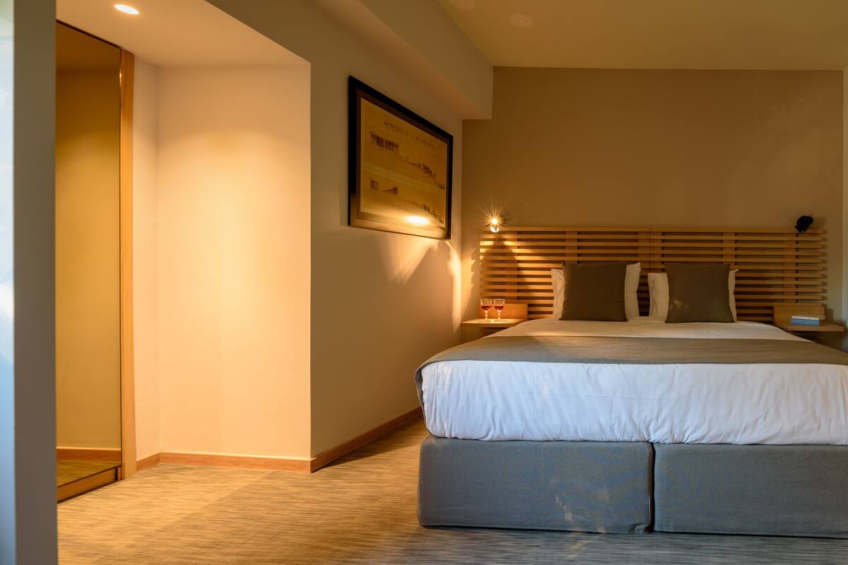 A modern hotel room with a large bed, a bedside table with a lamp, and a framed picture on the wall.