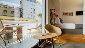 A modern hotel room with a balcony, a bed, a small table, and a chair. - Fos DownTown Suites (Athens)
