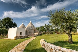 Un edificio de piedra con una cúpula central y dos cúpulas más pequeñas, rodeado de un césped cuidado y un sendero de piedra.