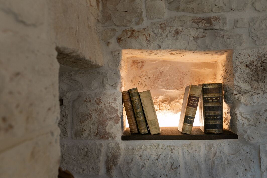 Paredes de pedra com uma prateleira exibindo vários livros antigos.