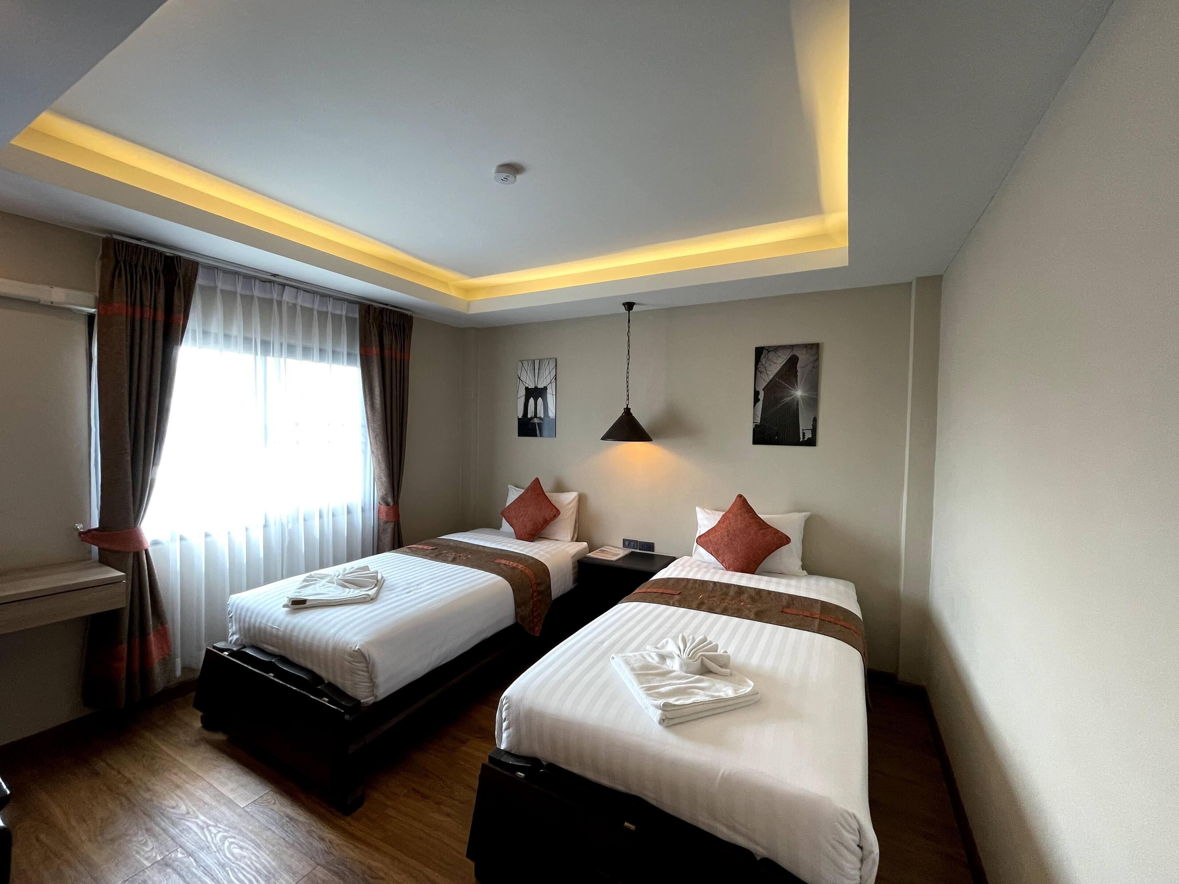A hotel room with two beds, a desk, and a window with curtains.