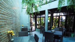 An outdoor patio area with wicker furniture and glass tables, surrounded by brick walls and large windows. - Fang Chiang Mai (Chiang Mai)