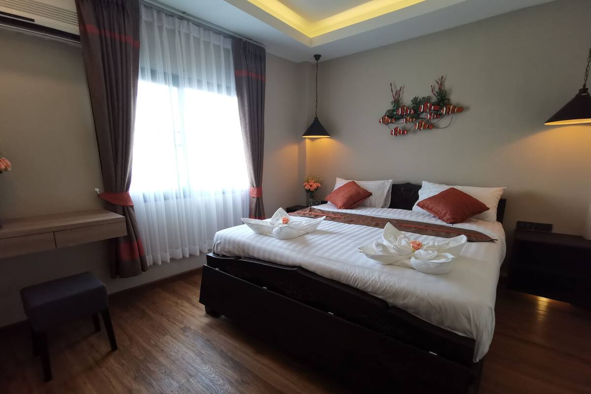 A neatly arranged hotel room with a large bed, bedside tables, a desk, and a window with curtains.