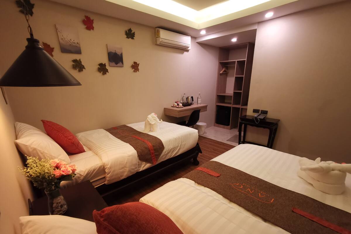 A hotel room with two beds, a desk, a chair, an air conditioning unit, and a small closet.