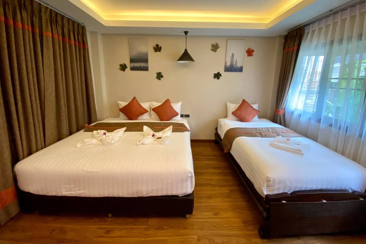A hotel room with two beds, each with white linens and brown headboards. There are decorative pillows, a ceiling light, and wall art including leaf motifs.