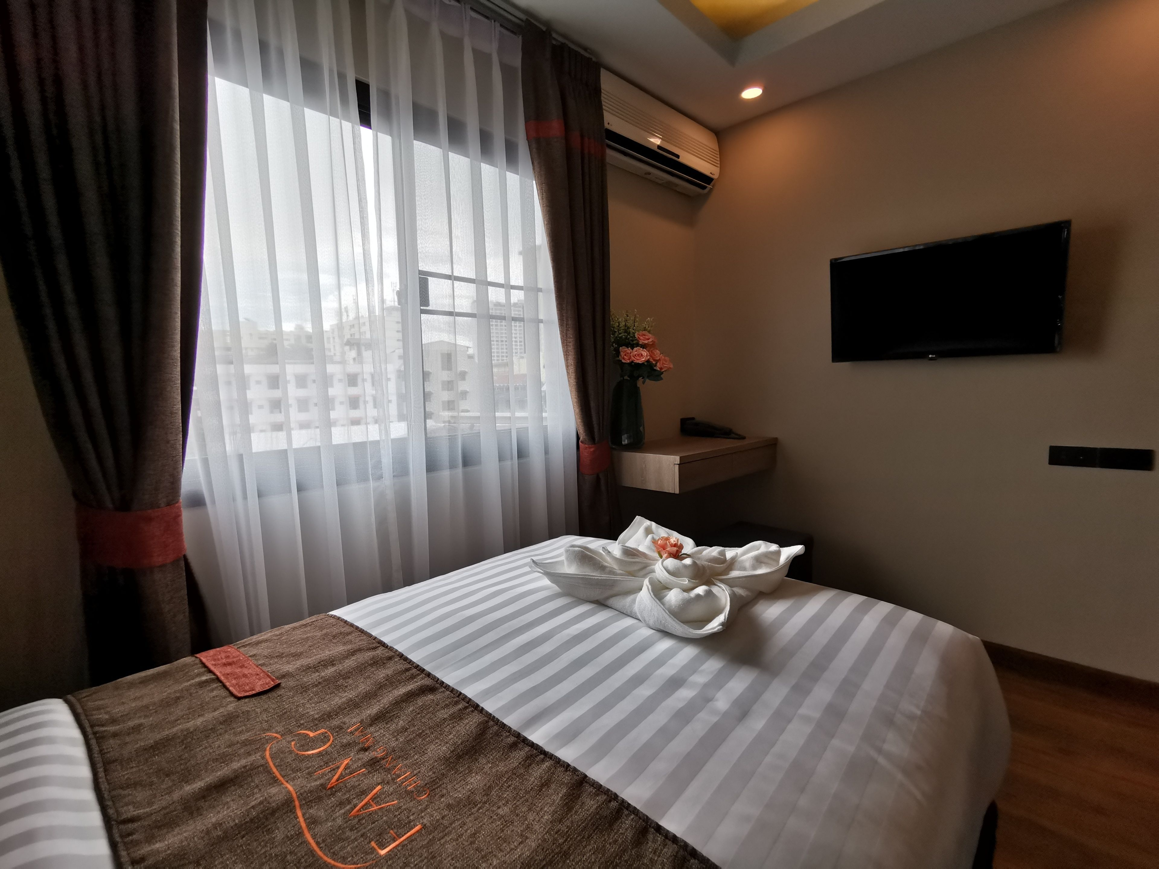 Una habitación de hotel con cama, televisión instalada en la pared y ventana con cortinas.