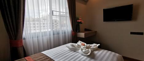 Una habitación de hotel con cama, televisión instalada en la pared y ventana con cortinas.