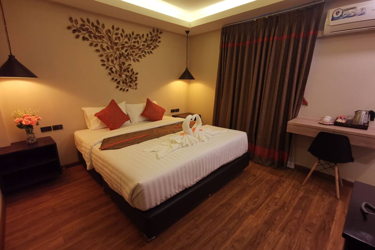 A hotel room with a bed, a desk, a chair, a vase with flowers, and a wall decoration.