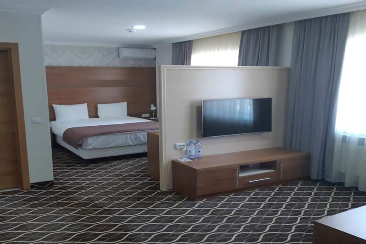 Una habitación de hotel con una cama, un televisor, un armario de madera y una alfombra estampada.