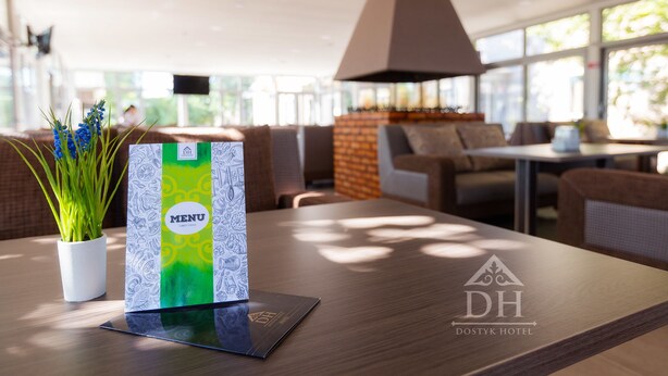 A modern hotel lobby with a wooden reception desk, a menu stand, and a potted plant. - Dostyk Hotel Bautino (Fort Shevchenko)