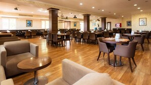 A spacious hotel lobby with multiple seating areas, including sofas and round tables, and a large dining area with numerous chairs. - Dostyk Hotel Bautino (Fort Shevchenko)