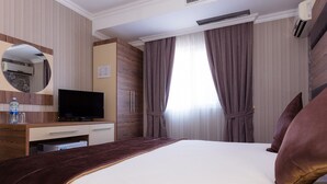 A hotel room with a bed, a flat-screen TV, a minibar, a mirror, and a window with curtains. - Dostyk Hotel Bautino (Fort Shevchenko)