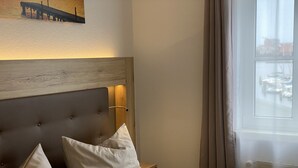 A neatly made bed with a wooden headboard, two pillows, and a light-colored bedspread.