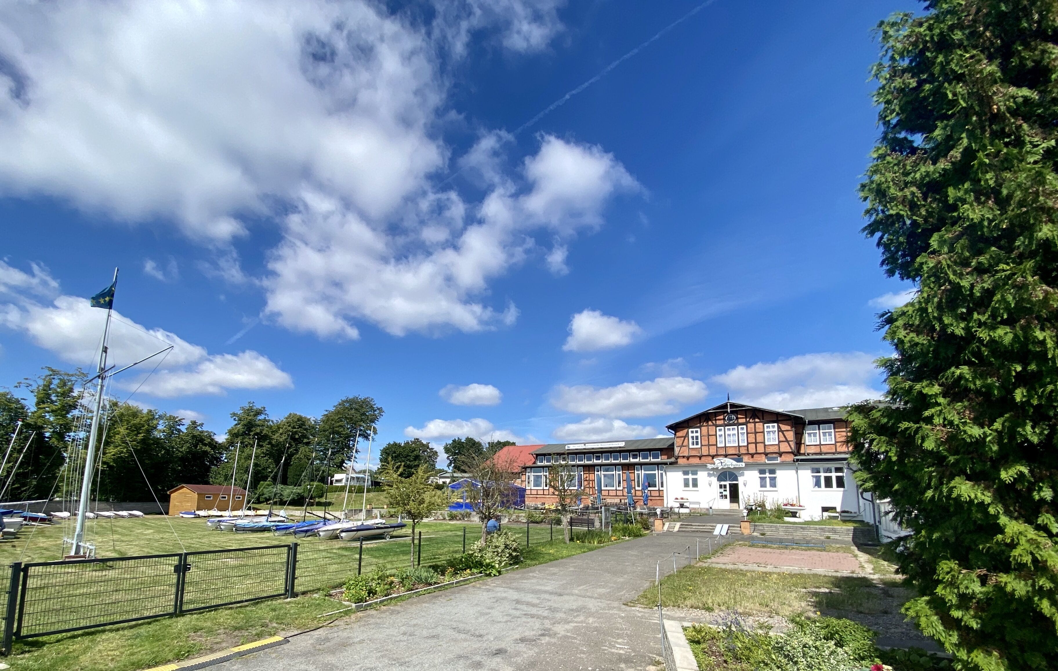 A building with a red and white facade, a grassy area with boats, and a clear blue sky.