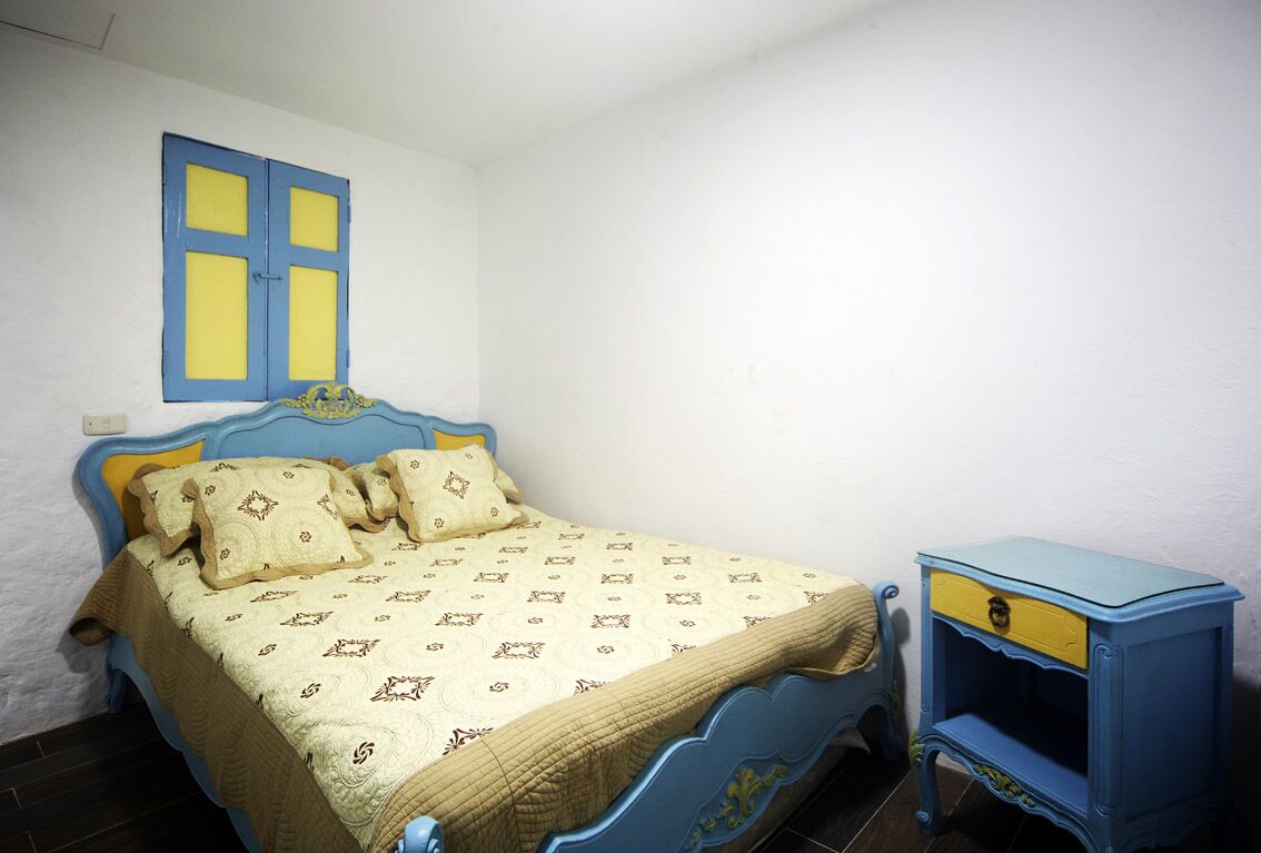 Un dormitorio con una cama, una mesita de noche y un ventanal con contraventanas azules.