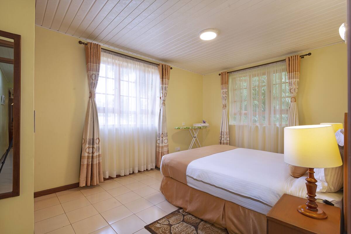 A hotel room with a bed, a nightstand with a lamp, a small table, and curtains.