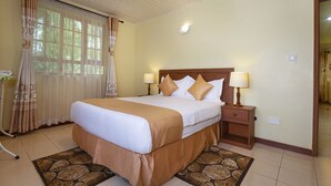 Quarto de hotel com uma cama grande, duas luminárias de cabeceira, mesa de cabeceira, janela com cortinas e luz acoplada à parede.