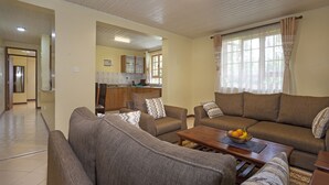 Sala de estar com sofá, uma mesa de centro com frutas e uma cozinha ao fundo.