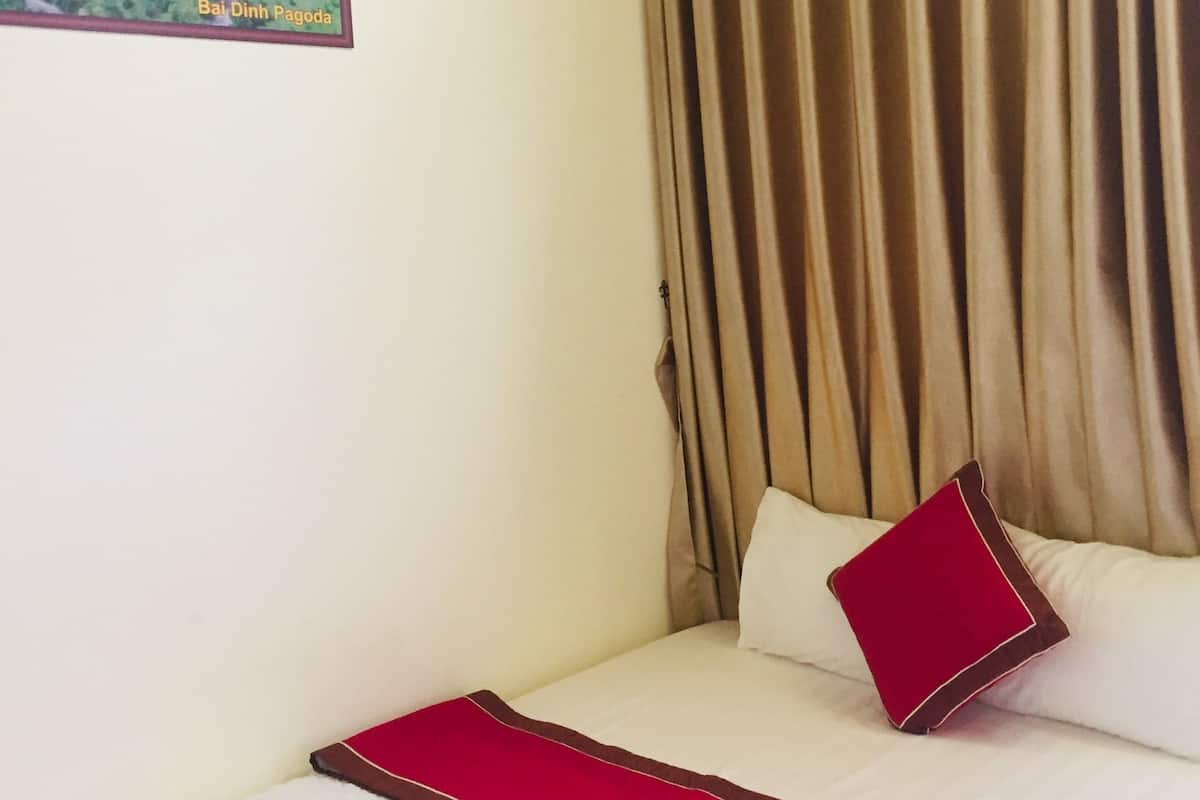 Hotelkamer met een bed, een rood kussen, beige gordijnen en een lijst met een foto van de Bai Dinh Pagoda.