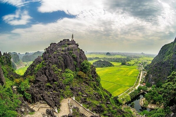 Un paysage montagneux avec un temple au sommet, une rivière et des champs verdoyants en contrebas.
